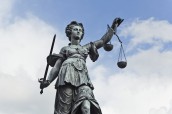 Statue of Justice with sword and scales in front of a blue cloudy sky