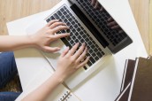 Top view of woman's hands working with laptop on white table.