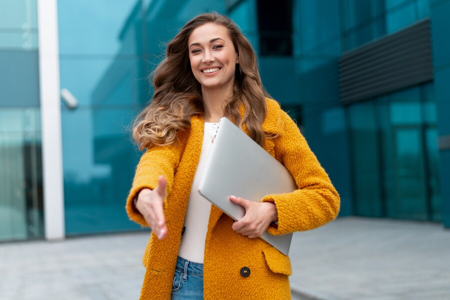 businesswoman-extend-hand-ready-handshake-greeting-client-business-partner-sign-deal-woman-hr-meeting-employee-interview-nice-meet-you-business-person-with-laptop-yellow-coat-standing-outdoors_91014-4556